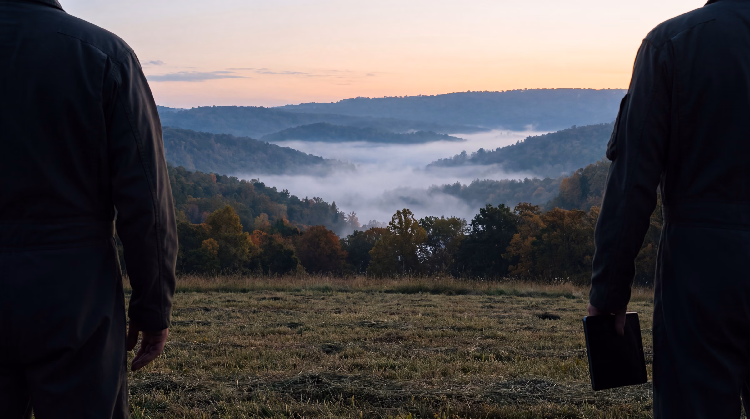 Illustrative: two pilots seen from behind, cropped at the shoulders, against a dawn sky over a hayfield