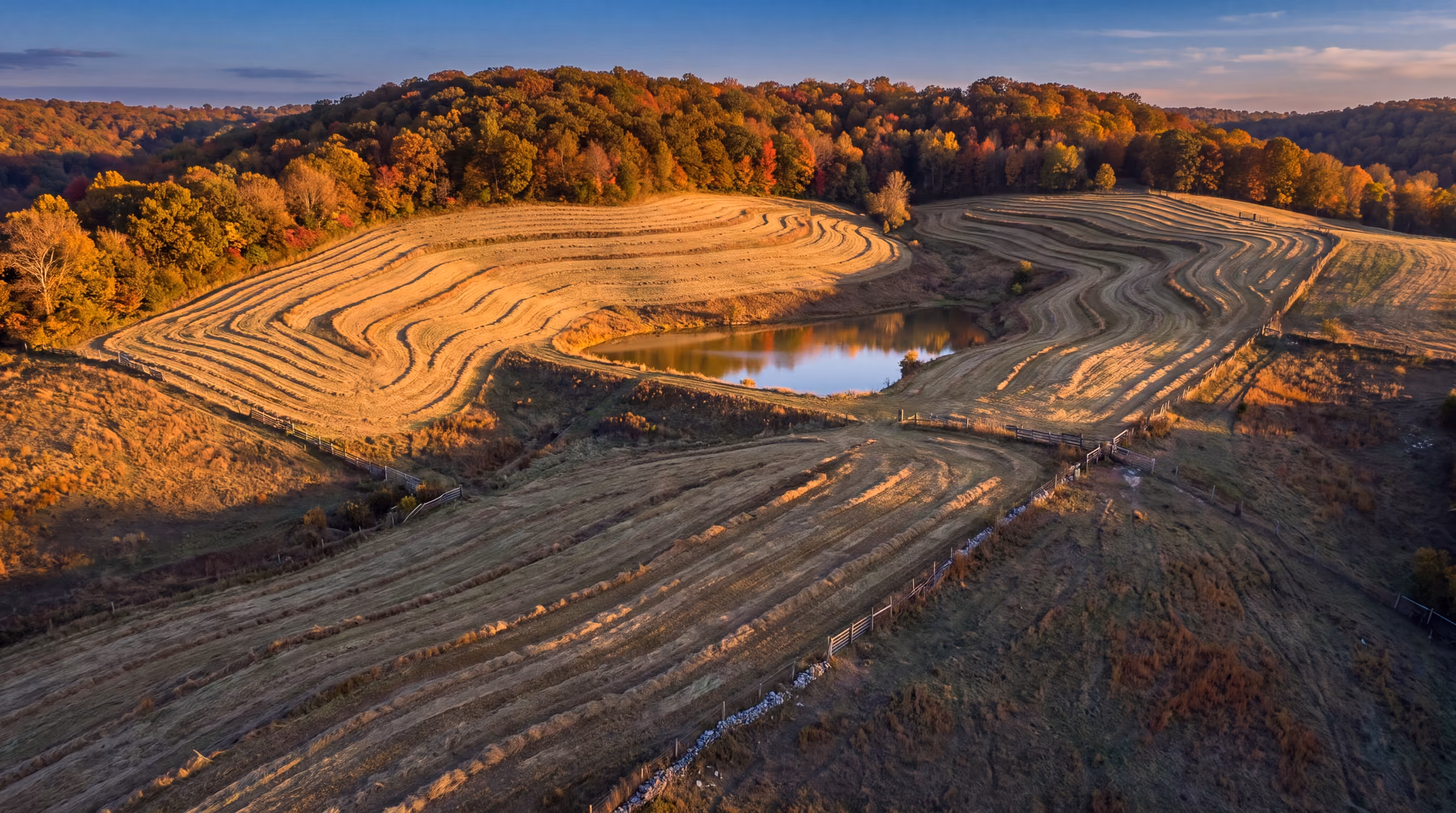 Illustrative: an oblique aerial view of terraced hillside hay fields and a farm pond at golden hour
