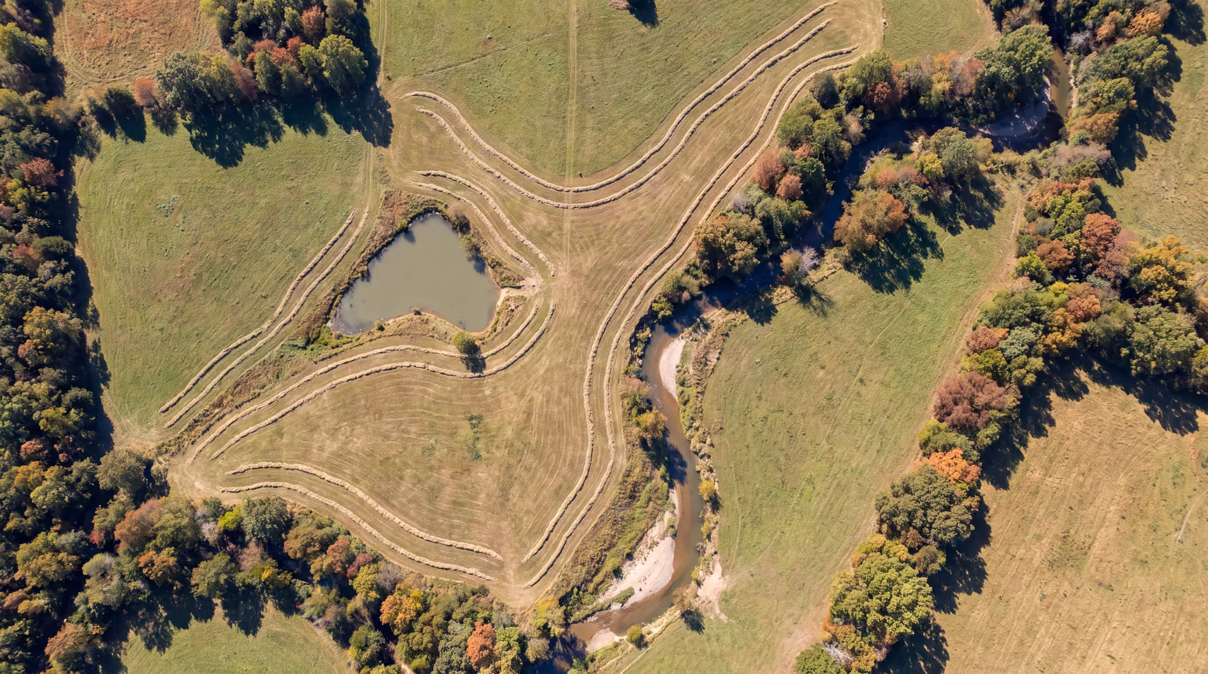 Illustrative: top-down aerial view of Ozark pasture, hay rows and a farm pond